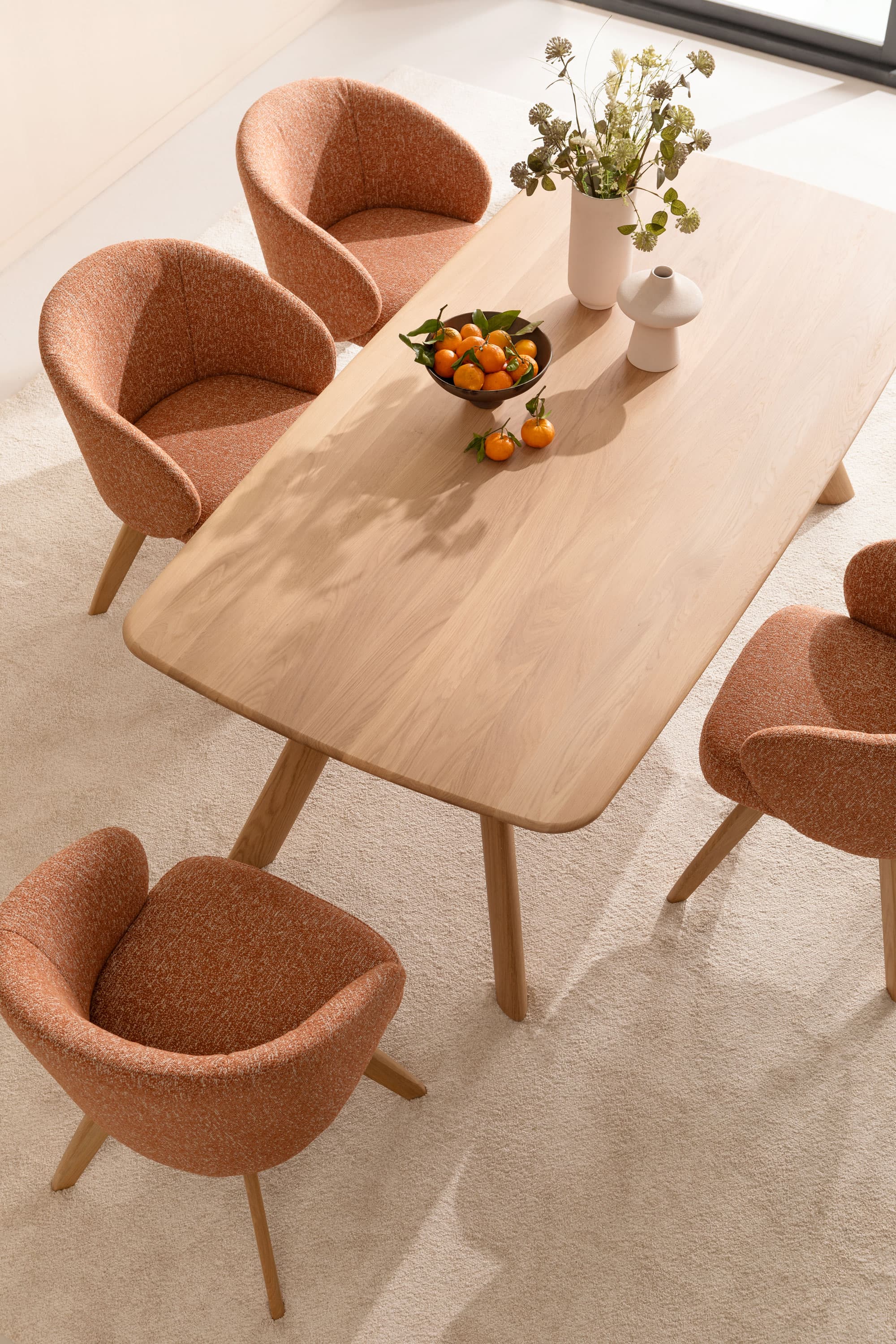 Holztisch mit vier gepolsterten Stühlen und einer Schüssel mit Orangen auf einem hellen Teppich.