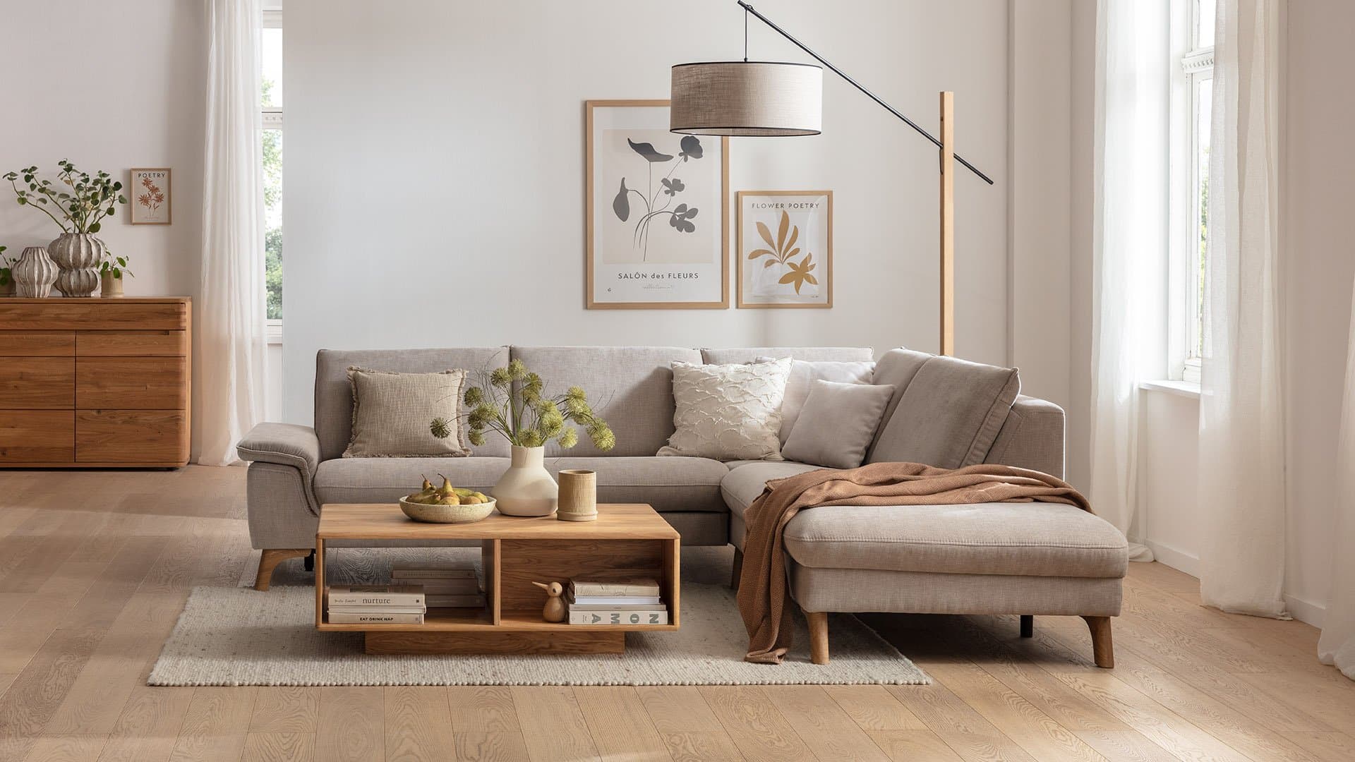 Helles Wohnzimmer mit beigem Ecksofa, Holzcouchtisch, natürlicher Dekoration und warmem Tageslicht.