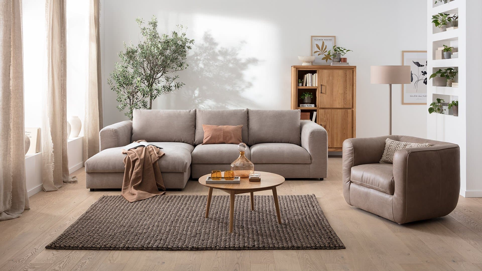 Moderne Wohnzimmerausstattung mit beigem Sofa, Cocktailsessel, Tisch und Pflanze, helles, einladendes Ambiente.