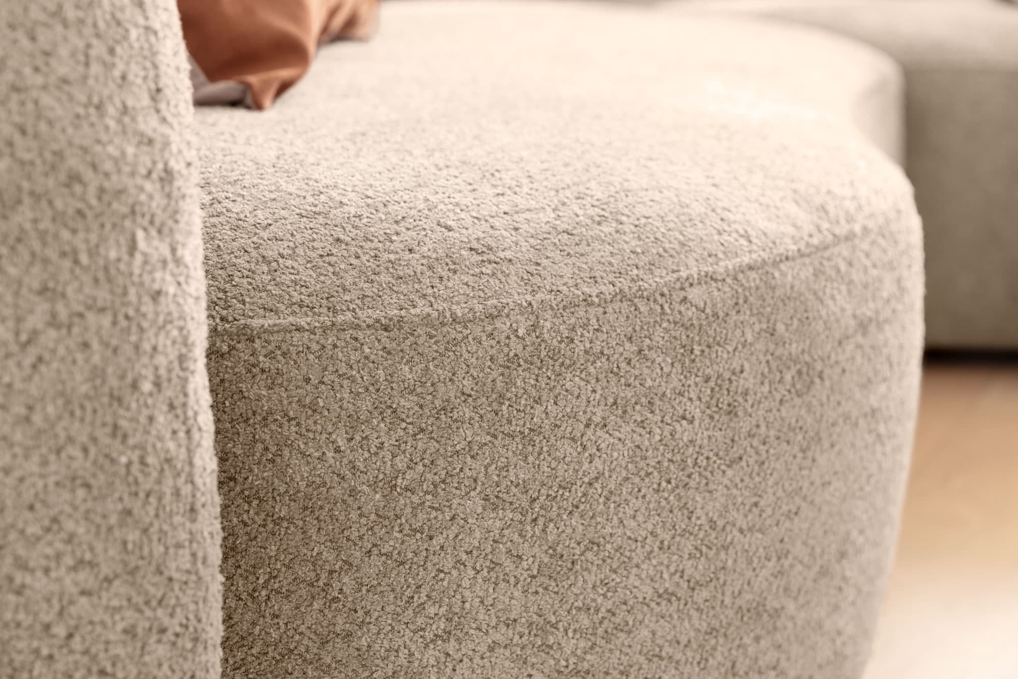 Beige, runde Sofakante mit einer weichen Textur und einem minimalistischen Design im Hintergrund.