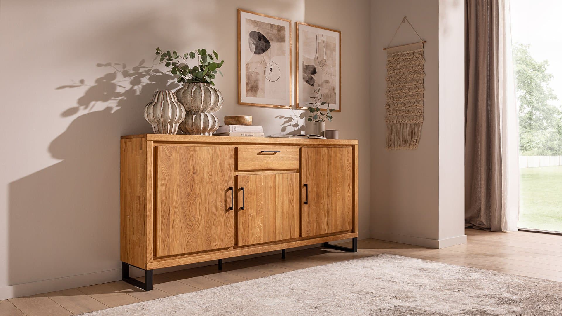 Holz-Schrank mit einer Schublade und zwei Türen, dekoriert mit Vasen und Bildern, in einem hellen Wohnraum.