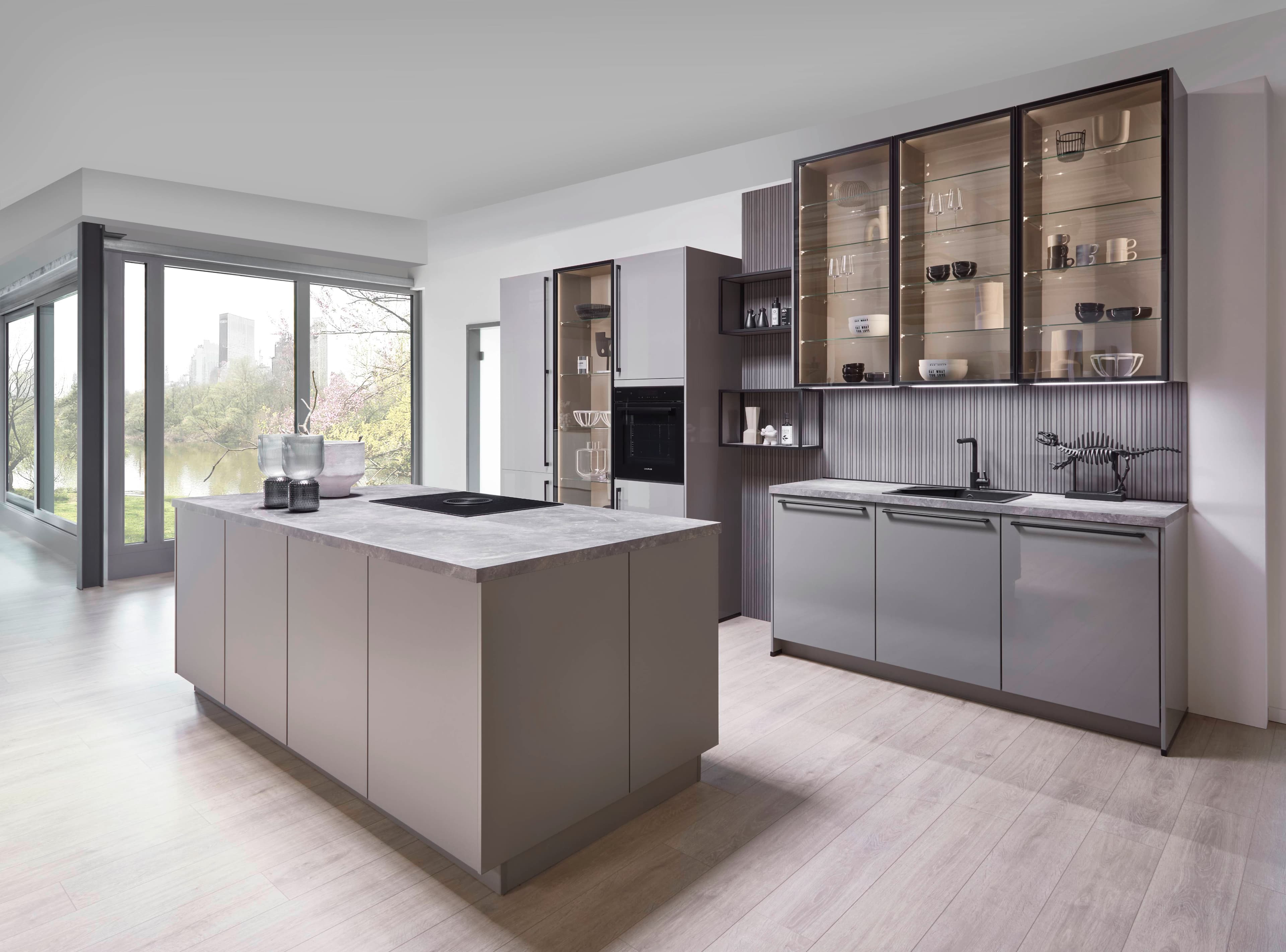 Moderne, helle Küche mit Insel, grauen Schränken und großen Fenstern, die natürliche Beleuchtung bieten.