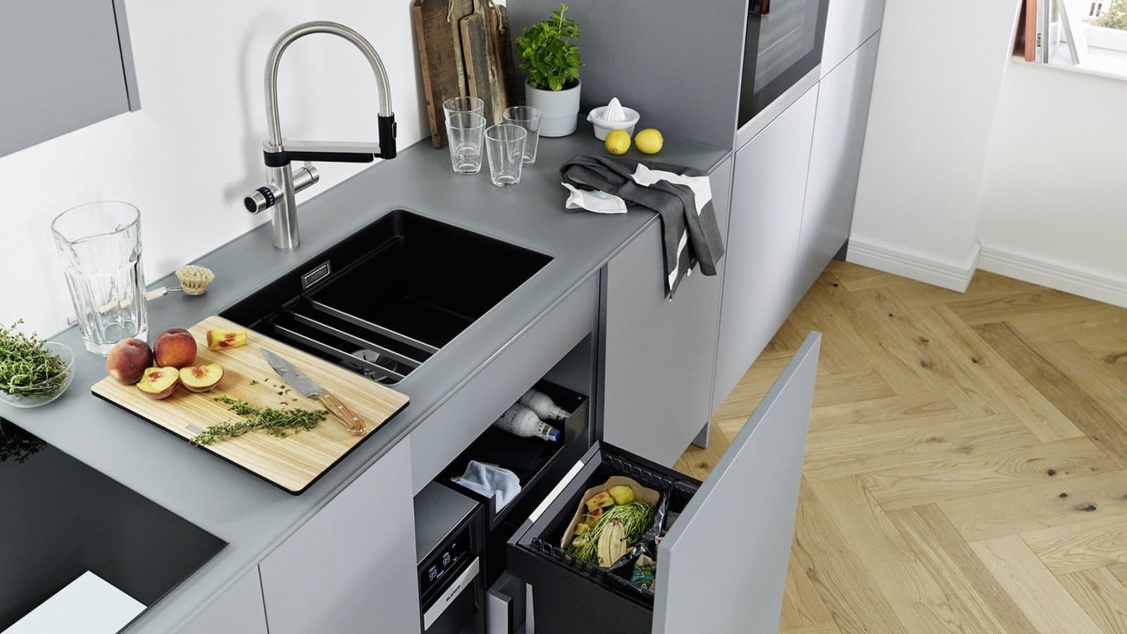 Moderne Küche mit grauen Schränken, schwarzem Spülbecken, einem Schneidebrett und Obst auf der Arbeitsplatte.