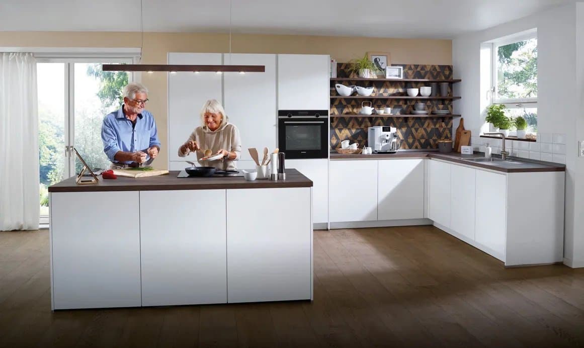 Ein älteres Ehepaar kocht zusammen in einer modernen, hellen Küche mit einer zentralen Kochinsel.