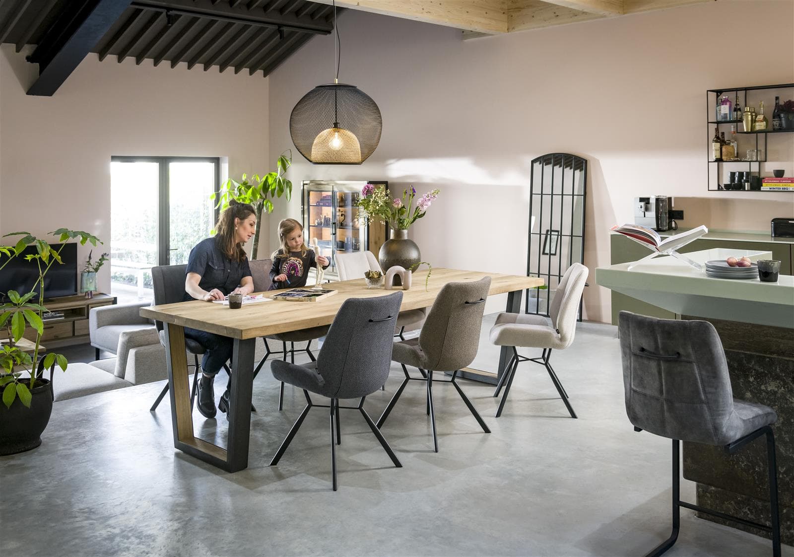 Modernes Esszimmer mit einem langen Tisch, Stühlen, Pflanzen und zwei Personen, die gemeinsam arbeiten oder essen.