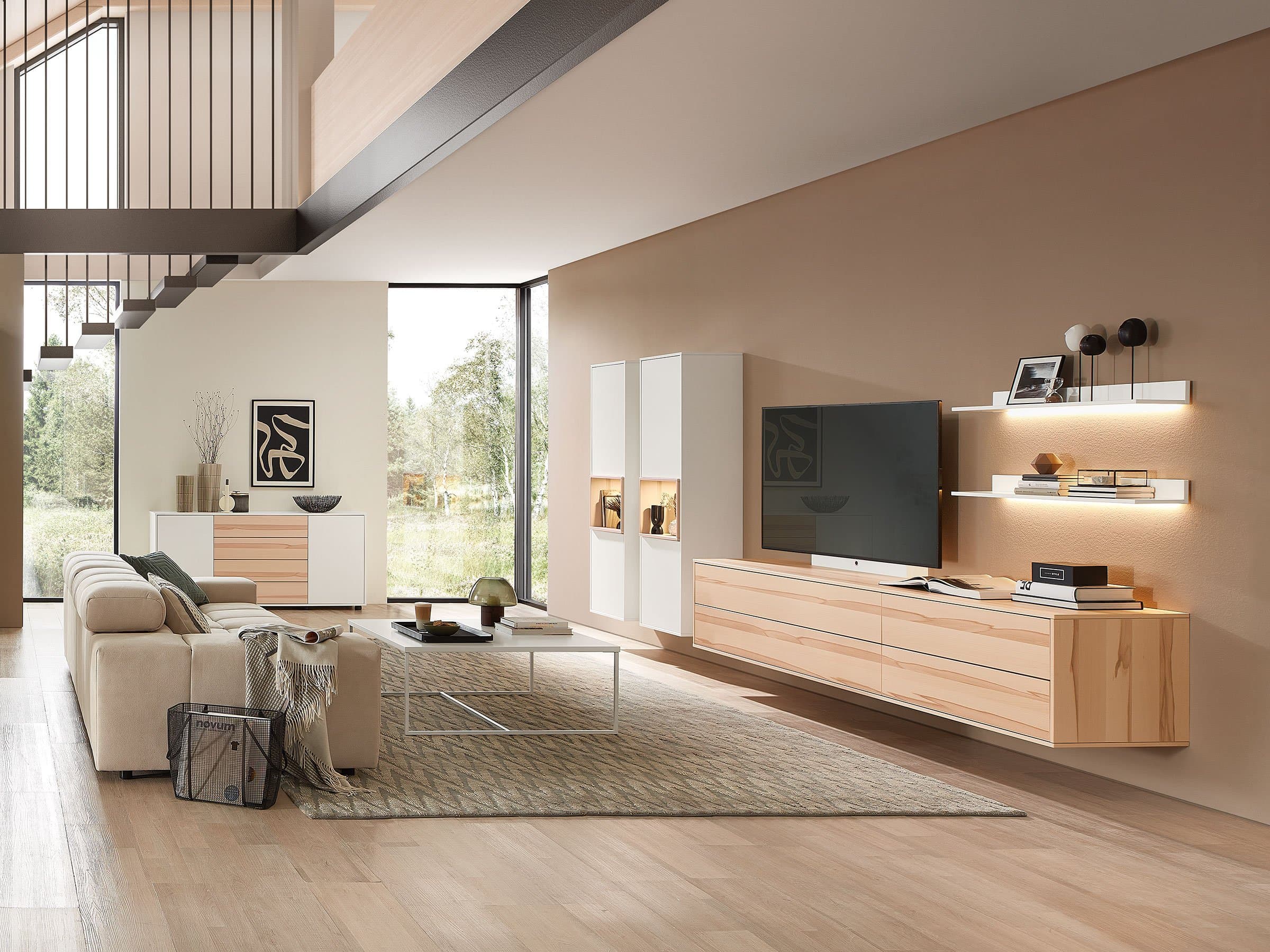 Modernes Wohnzimmer mit heller Wohnwand, Sofa, Couchtisch und großen Fensterfronten.