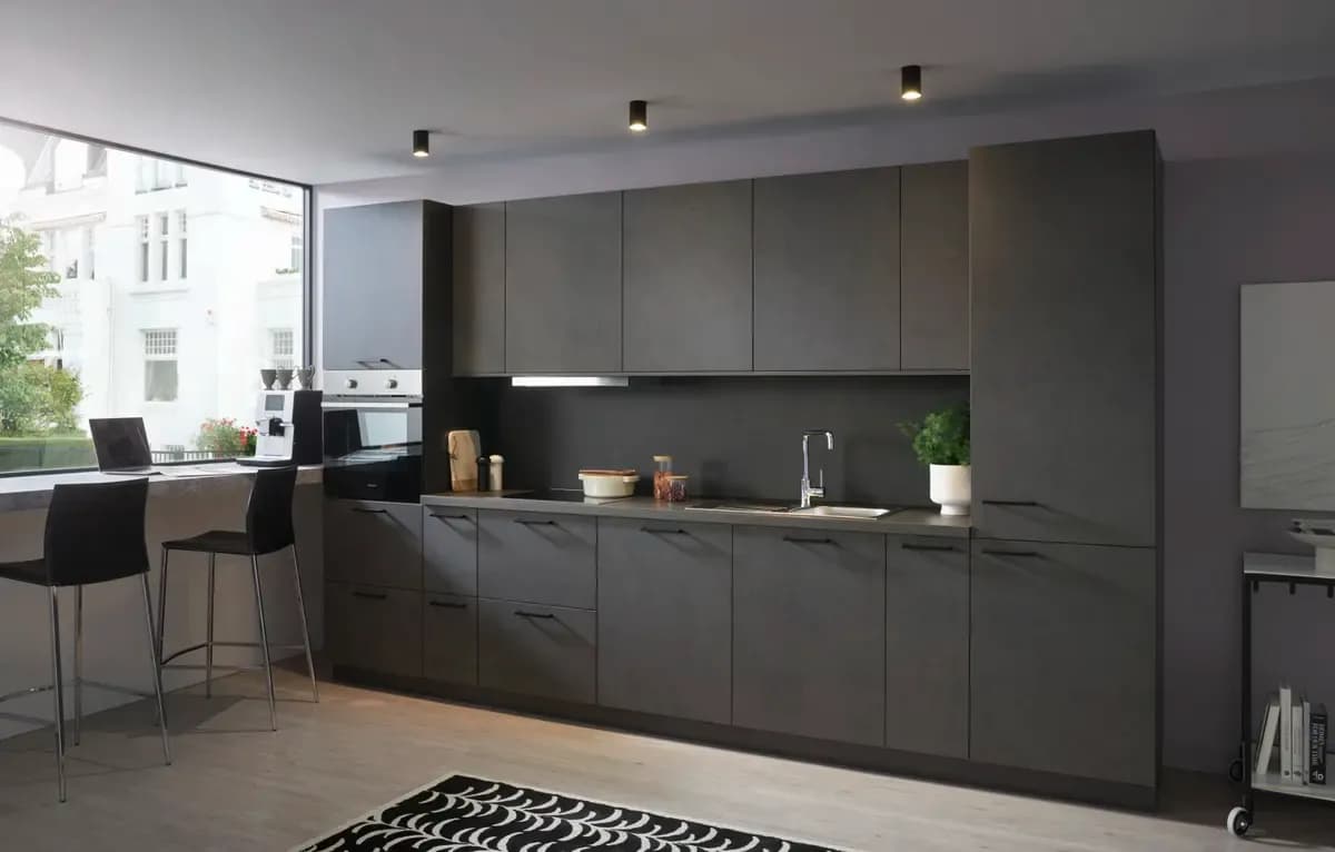 Moderne, minimalistische Küche in dunklen Tönen mit Fenster, Stühlen und Pflanzen. Helle Holzfußböden.