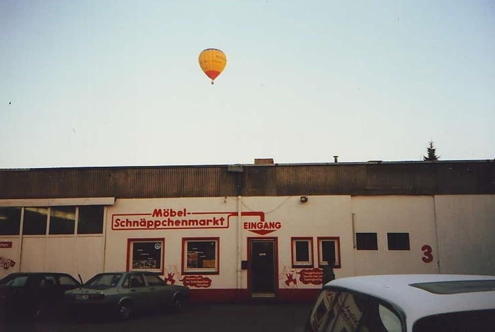Eine bunte Heißluftballon schwebt über einem Geschäft mit der Aufschrift „Mibal-Schnäppchenmarkt“.