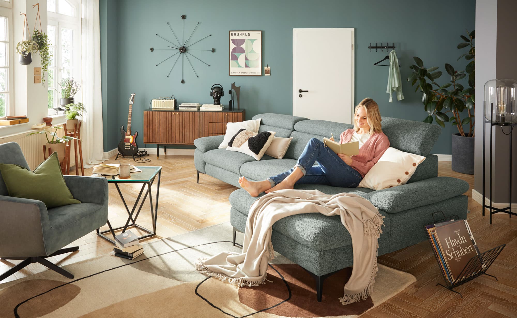 Gemütliches Wohnzimmer mit einer Frau auf einer blauen Couch, umgeben von Pflanzen und modernen Möbeln.