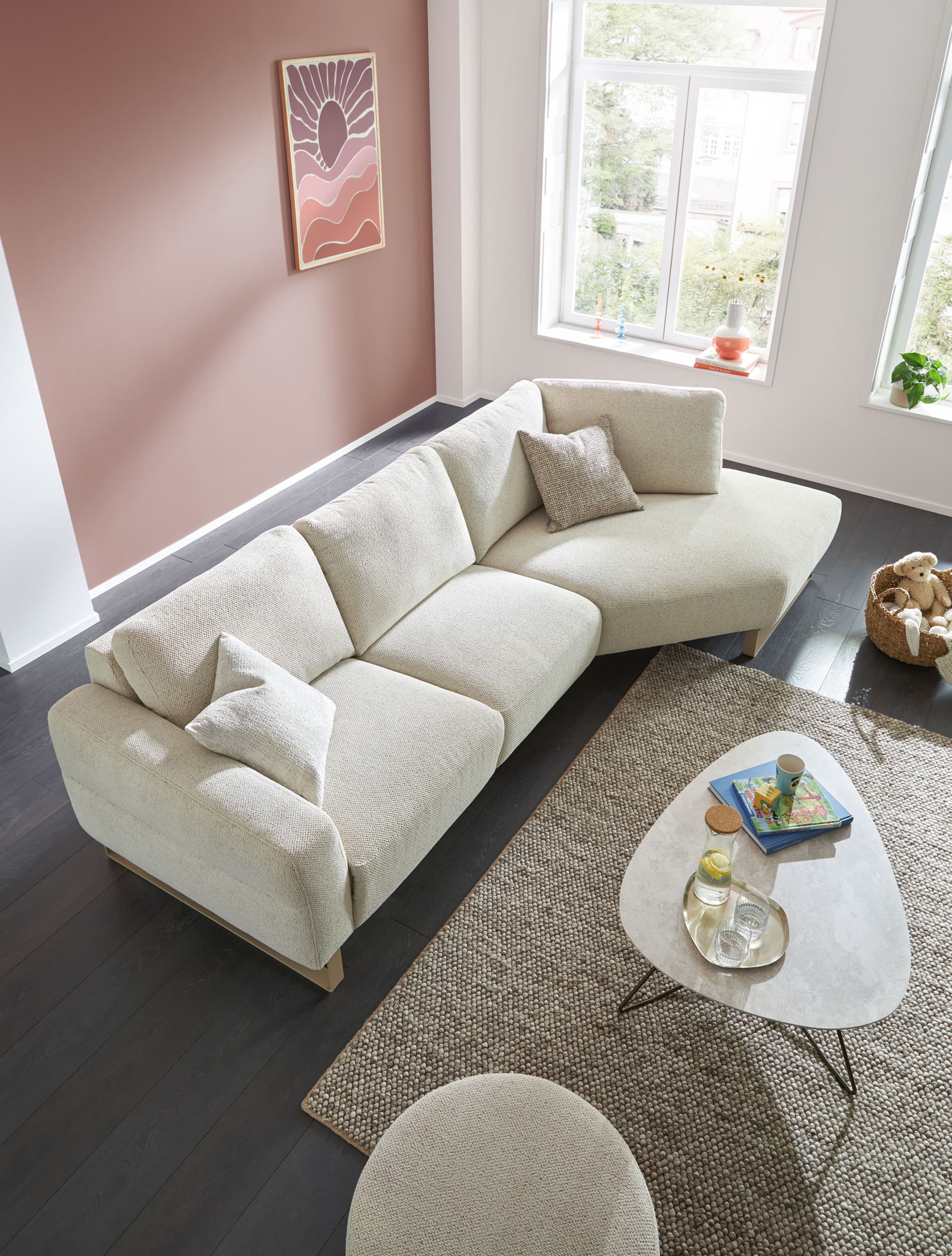 Helle Wohnlandschaft mit beigen Sofakissen, modernem Tisch und Kunstdruck an der Wand in einem lichtdurchfluteten Raum.