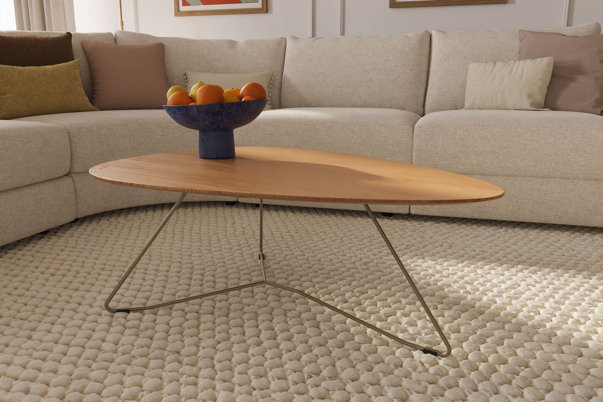 Ein ovaler Tisch mit Holzplatte und metallenen Füßen steht auf einem Teppich neben einer beigen Couch mit Kissen.
