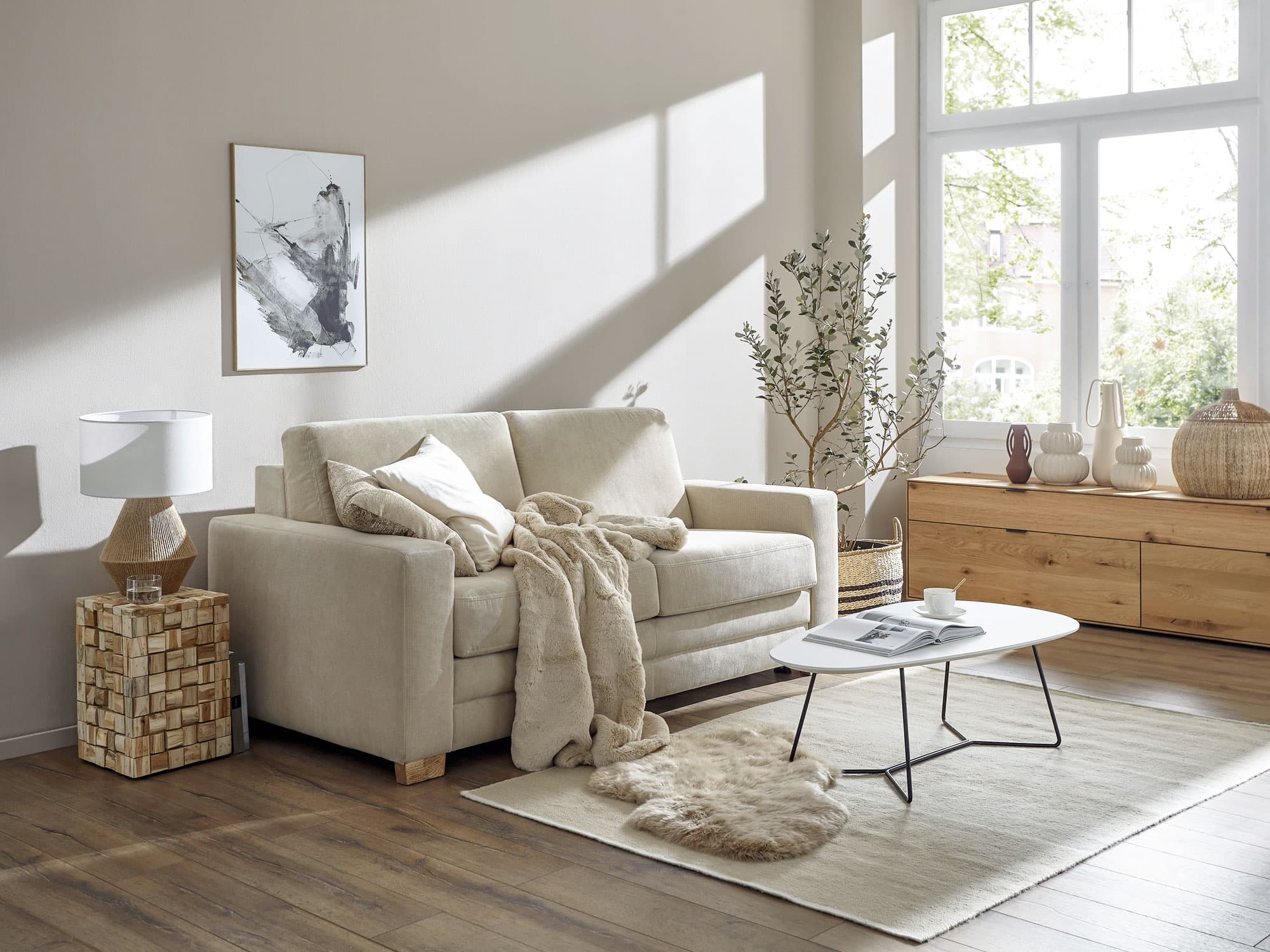 Helles Wohnzimmer mit lichtdurchfluteten Fenstern, einem beigen Sofa, einem Couchtisch und modernen Dekorationselementen.