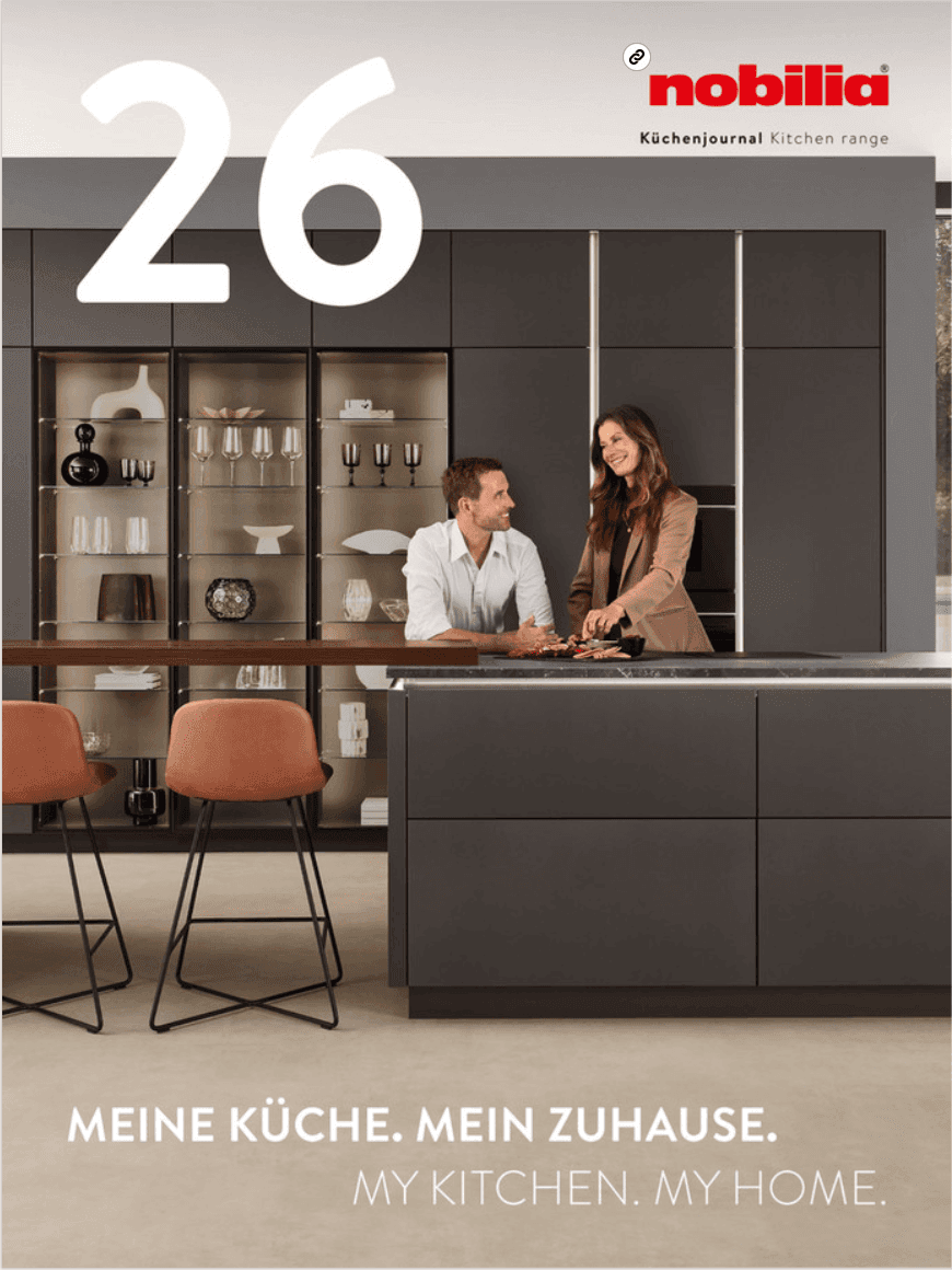 Prospekt-Titel nobilia Küchenjournal 26 „Meine Küche. Mein Zuhause.“ – dunkle Küche mit Kochinsel, beleuchteten Glasvitrinen, Barhockern und einem Paar
