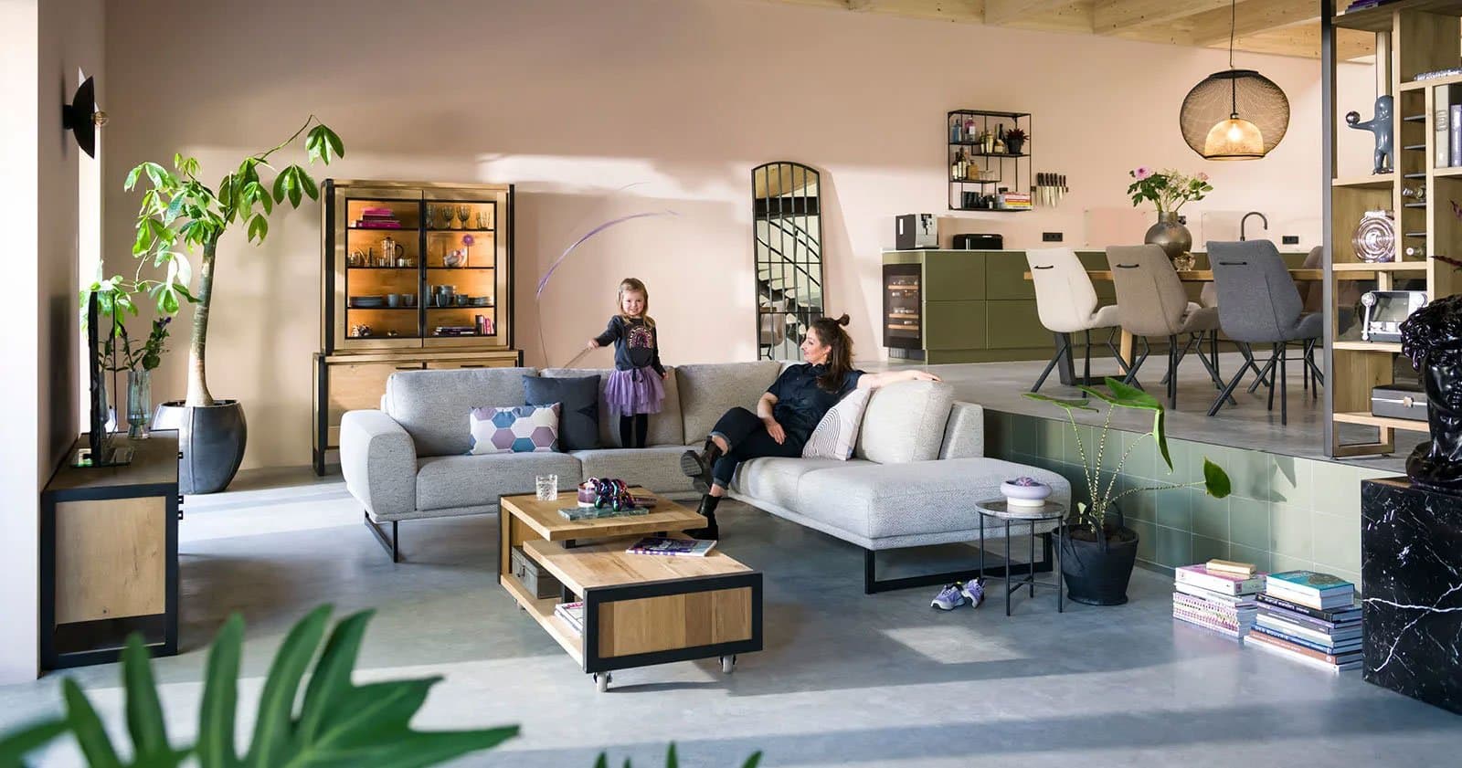 Modernes offenes Wohn-Esszimmer mit grauem Ecksofa, Holzmöbeln, Mutter und Kind